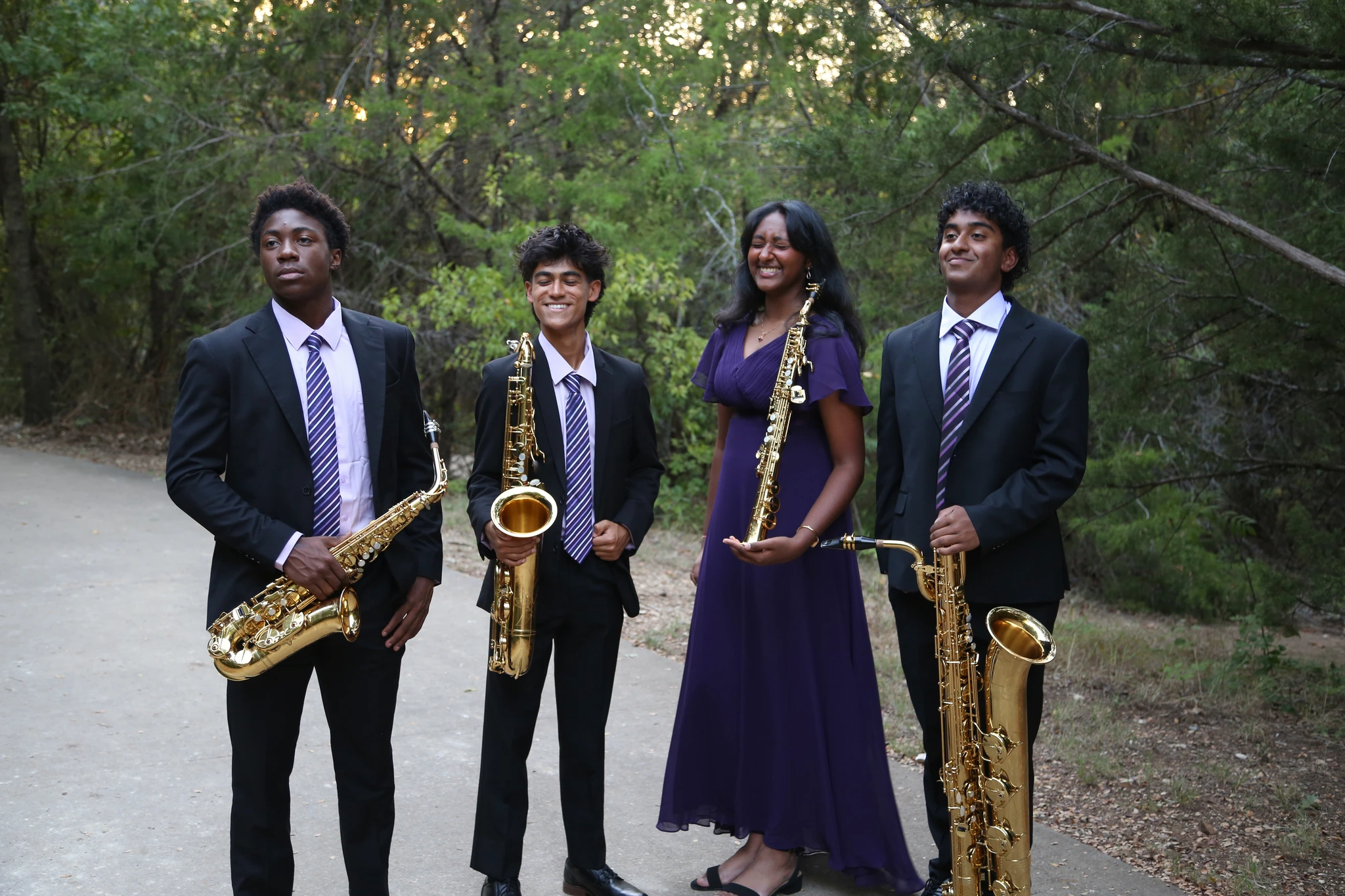 Orion Quartet smiling together with their saxophones on a woodland path