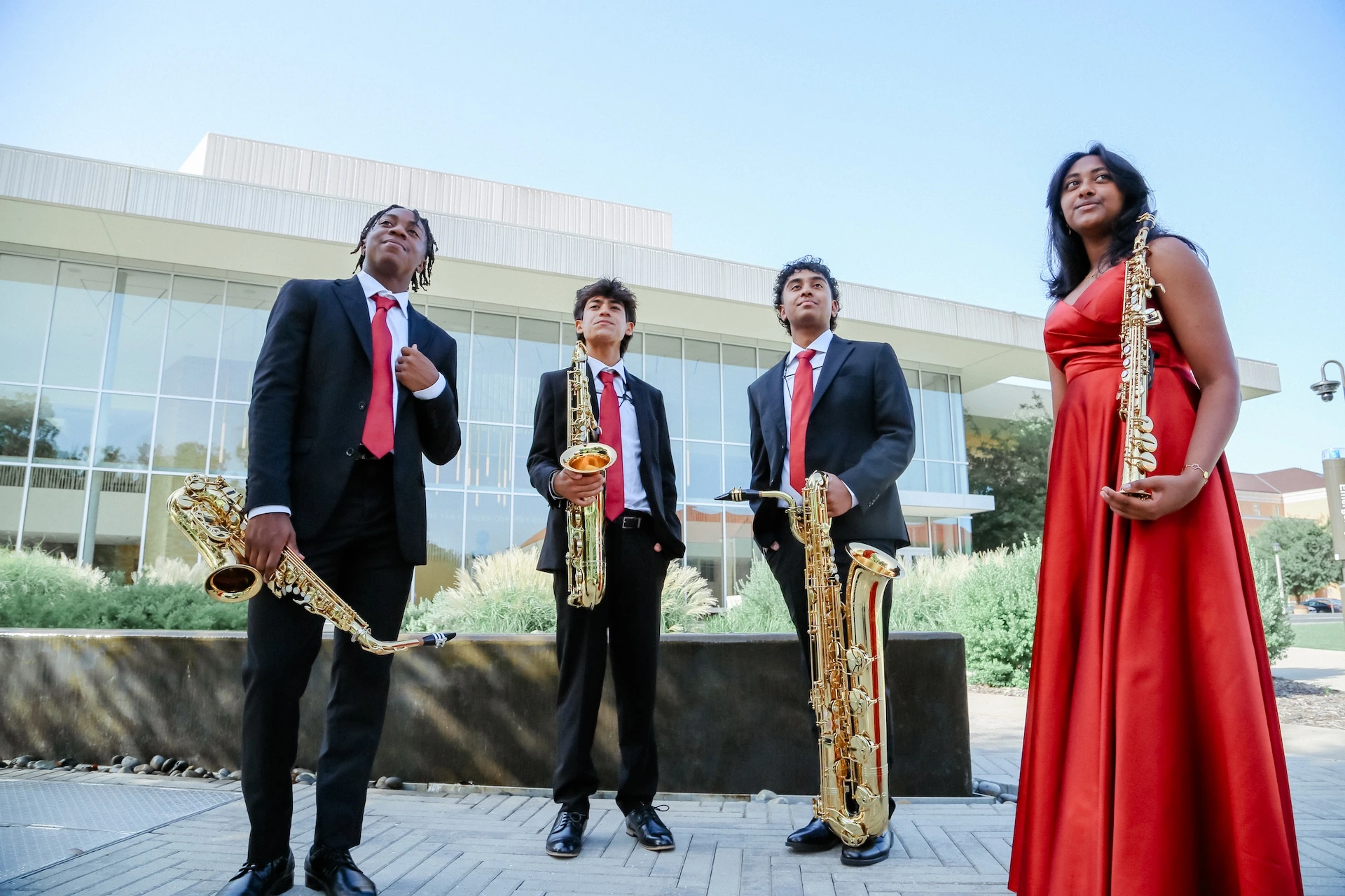 The four members of Orion Quartet pose outdoors with their saxophones, wearing coordinated black and red concert attire.